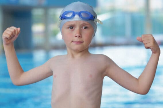 Vor dem Pool stehendes Kind mit Badekappe und Schwimmbrille