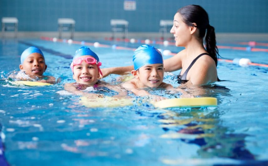 Drei Kinder im Pool, mit Schwimmhilfe und Schwimmlehrerin
