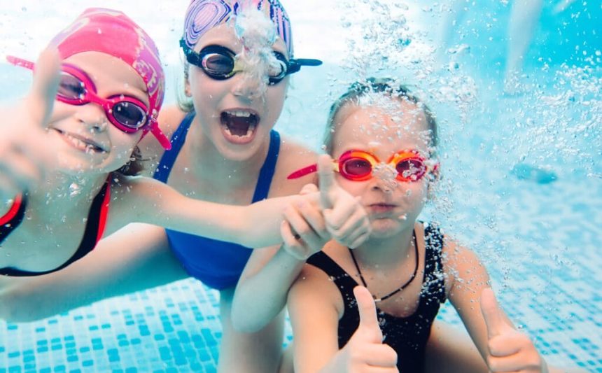 Drei im Pool tauchende Kinder, die die Daumen in die Luft strecken